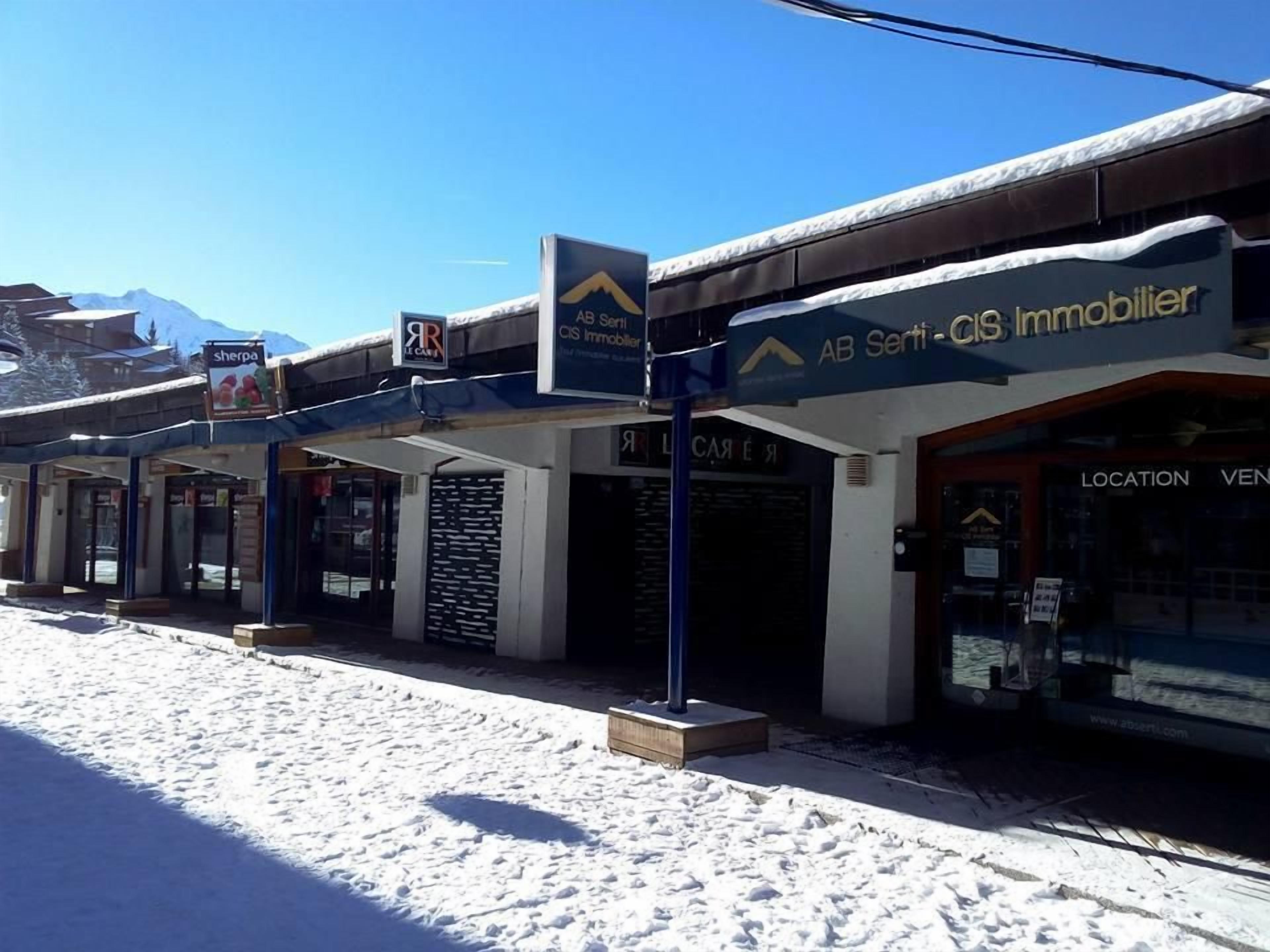 A row of commercial buildings with signage for 'AB Senti-CIS Immobilier' and 'Le Car'.