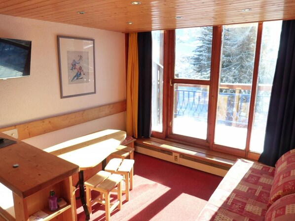 A room with a wooden bench, a table, and chairs, large windows with a view of trees, and a framed picture on the wall.