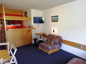 Una habitación pequeña con una cama nido, un sofá, una mesita, un televisor y un cuadro en la pared.