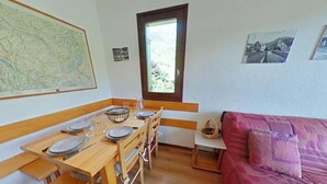 A cozy room with a wooden dining table set for four, a purple sofa, and a window with a view of greenery. - 1st floor, balcony, tv, 26m², Le Grand Bornand (Le Grand-Bornand)