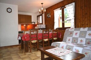A cozy room with a dining table set for four, a sofa, wooden walls, a kitchen area, and a clock on the wall. - 350m from resort center, 1st floor, balcony, tv, 43m², Le Grand Bornand (Le Grand-Bornand)