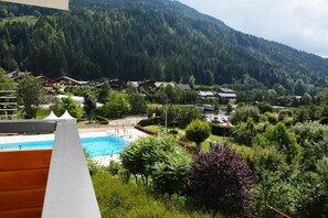 Vista de uma piscina rodeada por vegetação exuberante e casas numa região montanhosa.