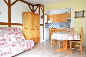 Una sala acogedora con sofá, mesa de comedor, armarios de madera y una cocina con baldosas a cuadros.
