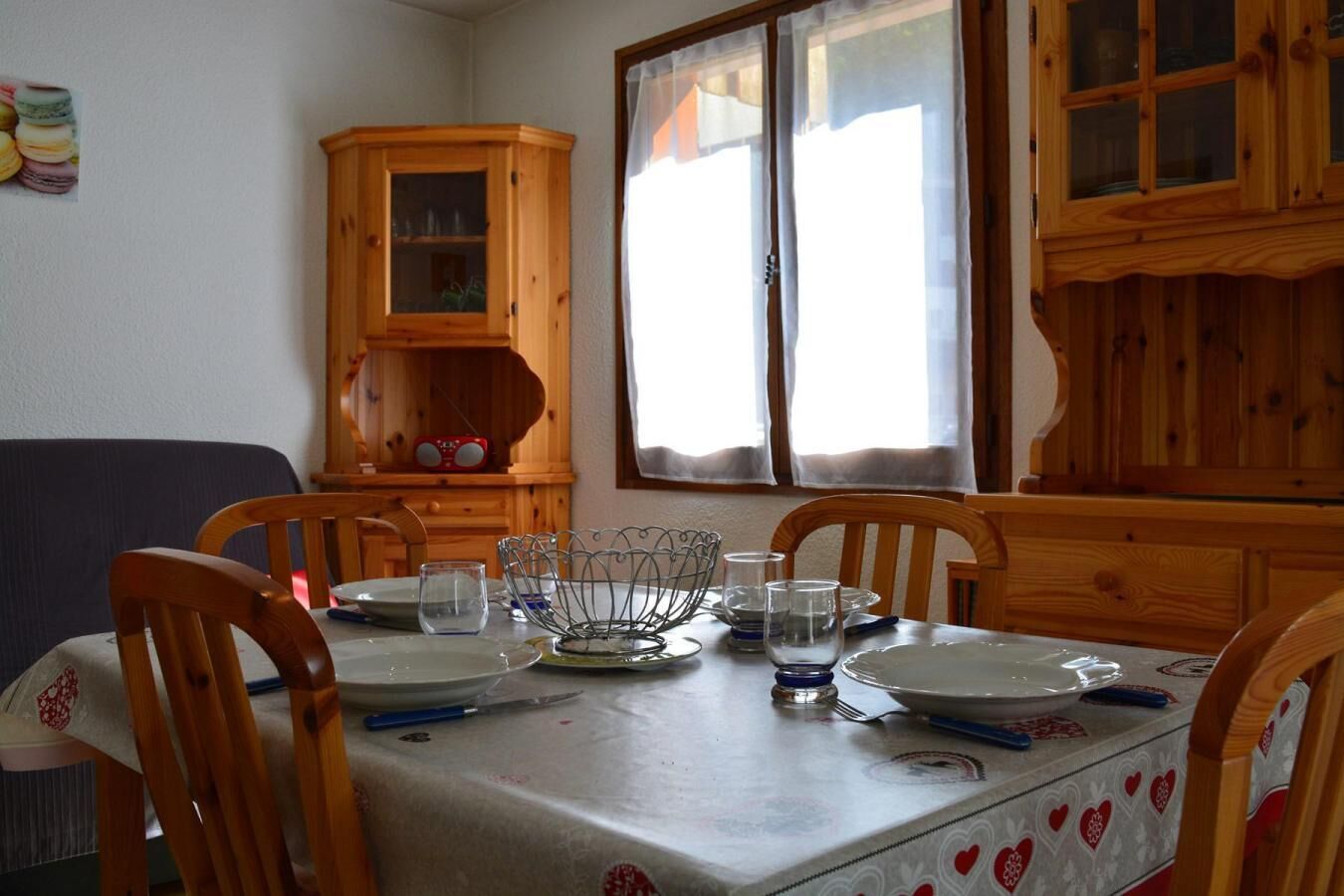 A dining table set with plates, glasses, and cutlery, surrounded by wooden chairs.