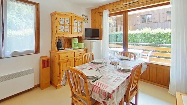 A dining area with a wooden table set for four, a wooden cabinet with kitchen appliances, and a television above the cabinet. - Ground floor, balcony, tv, 31m², Le Grand Bornand (Le Grand-Bornand)