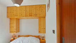 A bedroom with a wooden headboard, a bed with white bedding, two bedside tables with lamps, and a wooden door. - Ground floor, balcony, tv, 31m², Le Grand Bornand (Le Grand-Bornand)