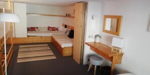 Une petite pièce comprenant un lit, un bureau, une chaise et un petit tabouret.