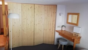 A room with a wooden wardrobe, a desk with a chair, a lamp, and a mirror on the wall. - 150m from resort center, 3rd floor, tv, 33m², Les Arcs (Les Arcs)