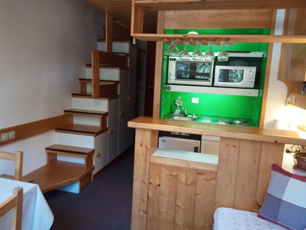 Una cocina compacta con salpicadero verde, armarios de madera y microondas integrado.