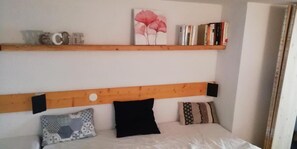 Un dormitorio con cabecera de madera, cama con ropa de cama blanca y estante con libros y adornos.