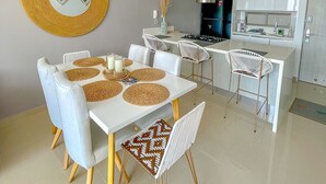 Una cocina moderna con armarios blancos, una campana extractora de acero inoxidable y una zona de comedor con mesa y sillas blancas.