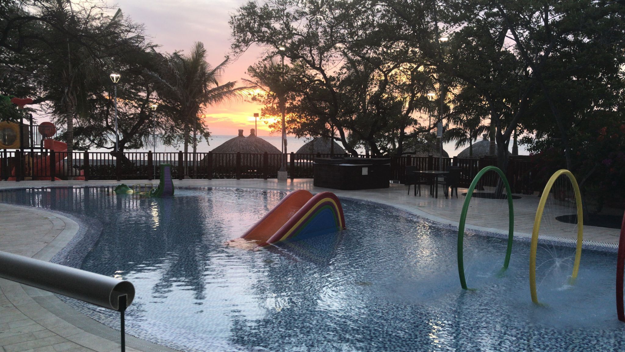 A swimming pool with slides and a sunset in the background.