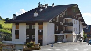 Ein mehrstöckiges Gebäude mit Satteldach, Balkonen und einer Parkfläche davor.