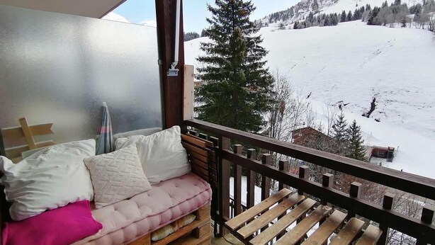 Ein Balkon mit einer hölzernen Sitzbank und einer gepolsterten Sitzecke mit Kissen.