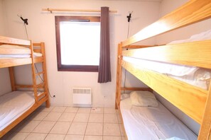 A small, clean room with two bunk beds, a window with curtains, a radiator, and a power outlet.