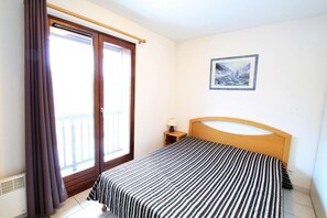 Een slaapkamer met een bed, nachtkastje, gordijnen voor het raam en een lijst aan de muur.