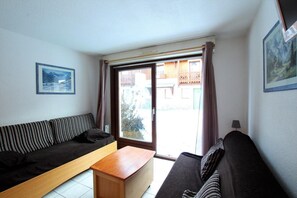 Een kleine woonkamer met een bank, een houten salontafel en een schuifdeur die leidt naar een buitenruimte.