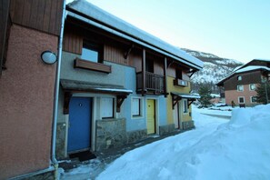 A multi-story building with a wooden balcony, stone foundation, and a blue door.