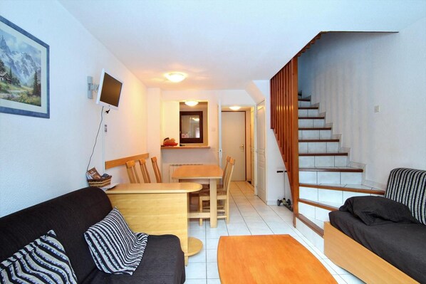 A compact living space with a dining area, two sofas, a staircase, and a painting on the wall.