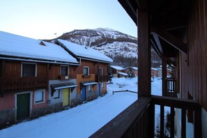 A snow-covered village with wooden buildings, a wooden balcony, and a mountain in the background.