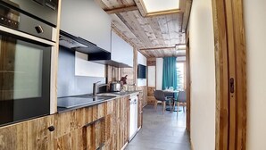 A modern kitchen with wooden cabinetry and a central island, a dining area with a table and chairs, and a view of the outdoors through a window. - 200m from ski slopes, Ground floor, terrace, tv, 42m², Les Menuires (Les Menuires)