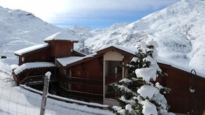 A wooden chalet with a balcony, surrounded by snow-covered mountains. - 100m from shops, 7th floor, balcony, tv, ski locker, 30m², Les Menuires (Les Menuires)