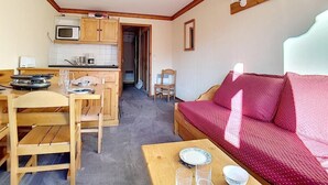 A compact room with a wooden dining table, chairs, a red sofa, a small kitchen area with a microwave and kettle, and a single bed. - 100m from shops, 7th floor, balcony, tv, ski locker, 30m², Les Menuires (Les Menuires)