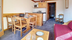 A compact room with a wooden dining table, chairs, a small kitchen area with a microwave, and a bed with a red cover. - 100m from shops, 7th floor, balcony, tv, ski locker, 30m², Les Menuires (Les Menuires)
