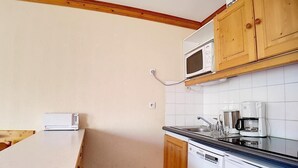 A kitchen with wooden cabinets, a microwave, a coffee maker, and a dishwasher. - 100m from shops, 7th floor, balcony, tv, ski locker, 30m², Les Menuires (Les Menuires)
