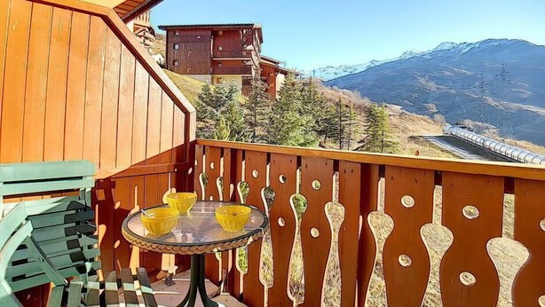 A wooden balcony with a table and chairs, overlooking a mountainous landscape and a train track. - 100m from shops, 7th floor, balcony, tv, ski locker, 30m², Les Menuires (Les Menuires)