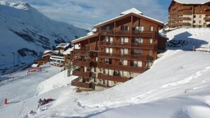 Een meerlaags houten gebouw met balkons, gelegen op een besneeuwde berghelling.