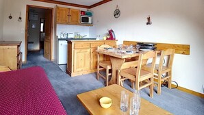 Een compacte keuken met houten kastjes, een magnetron en een eethoek met een tafel en stoelen.