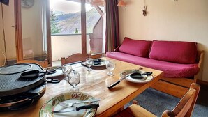 Een eetruimte met een houten tafel voor vier personen, een rode bank en uitzicht op bergen door grote ramen.