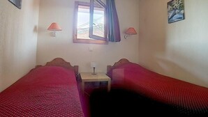 Een kamer met twee bedden, elk voorzien van een rode sprei, een klein nachtkastje met een lamp en een raam met gordijnen.