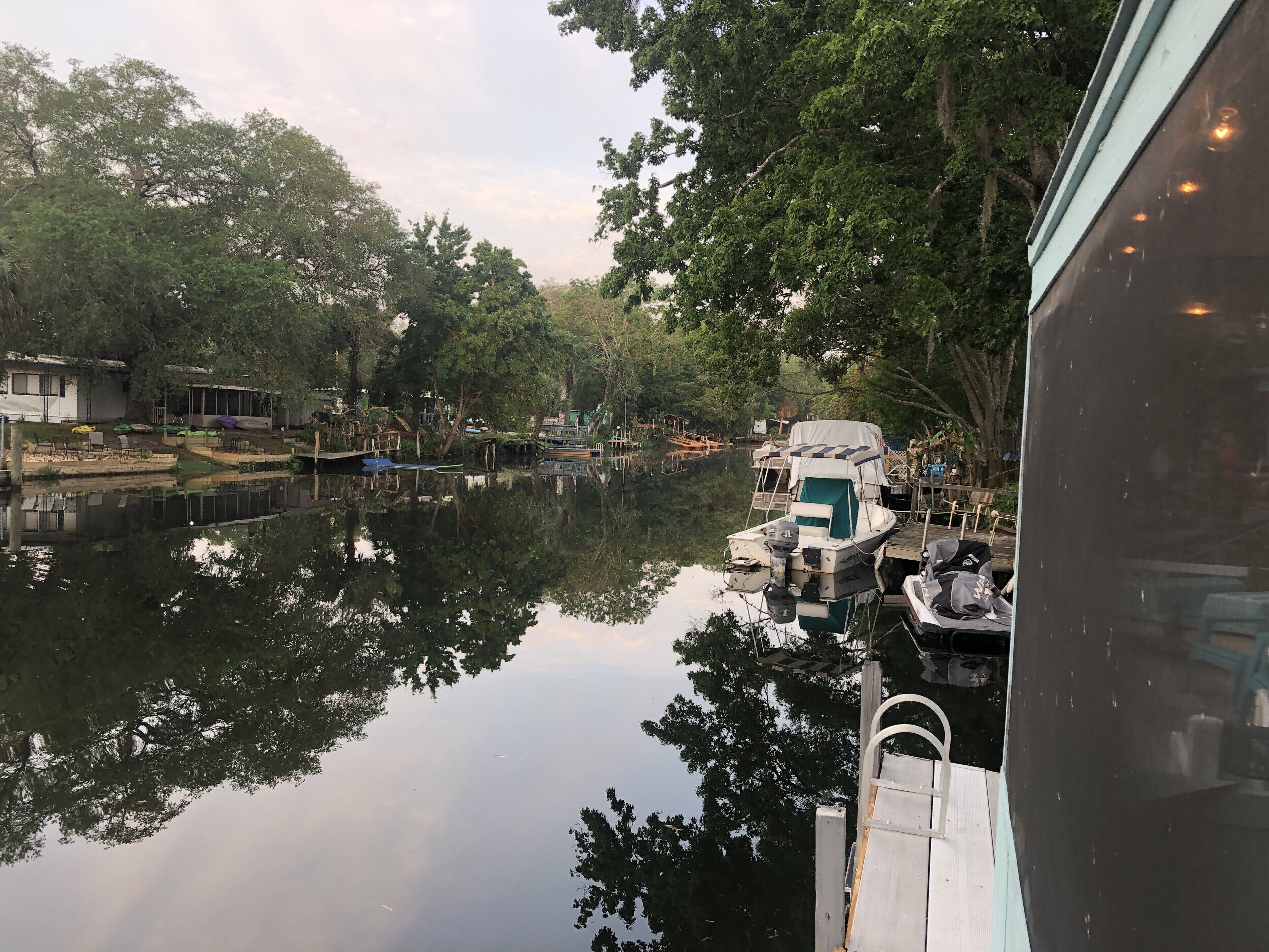 A calm river with boats docked on the right, surrounded by trees and a small dock area.