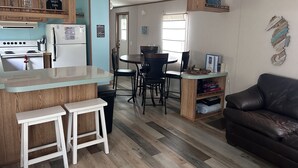 Una cocina compacta con refrigerador, estufa y taburetes de bar. Hay un comedor con mesa y sillas, y una sala de estar con sofá.