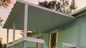 Un edificio azul claro con un porche cubierto y una escalera que lleva a una puerta con un ventanal en forma de rombo.