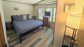 Un dormitorio con cama, cómoda, televisor y ventana con persianas.