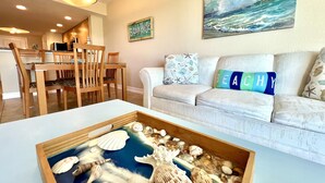 Ein Wohnzimmer mit Essbereich, einem Strandbild und einer dekorativen Tablett mit Meeresschalen.