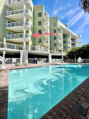 A hotel with a swimming pool, multiple balconies, and a clear blue sky.