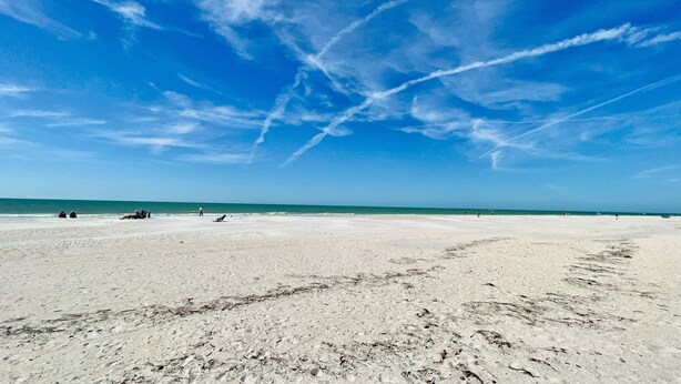 Ein weiter Sandstrand mit blauem Himmel und Blick auf den Ozean.