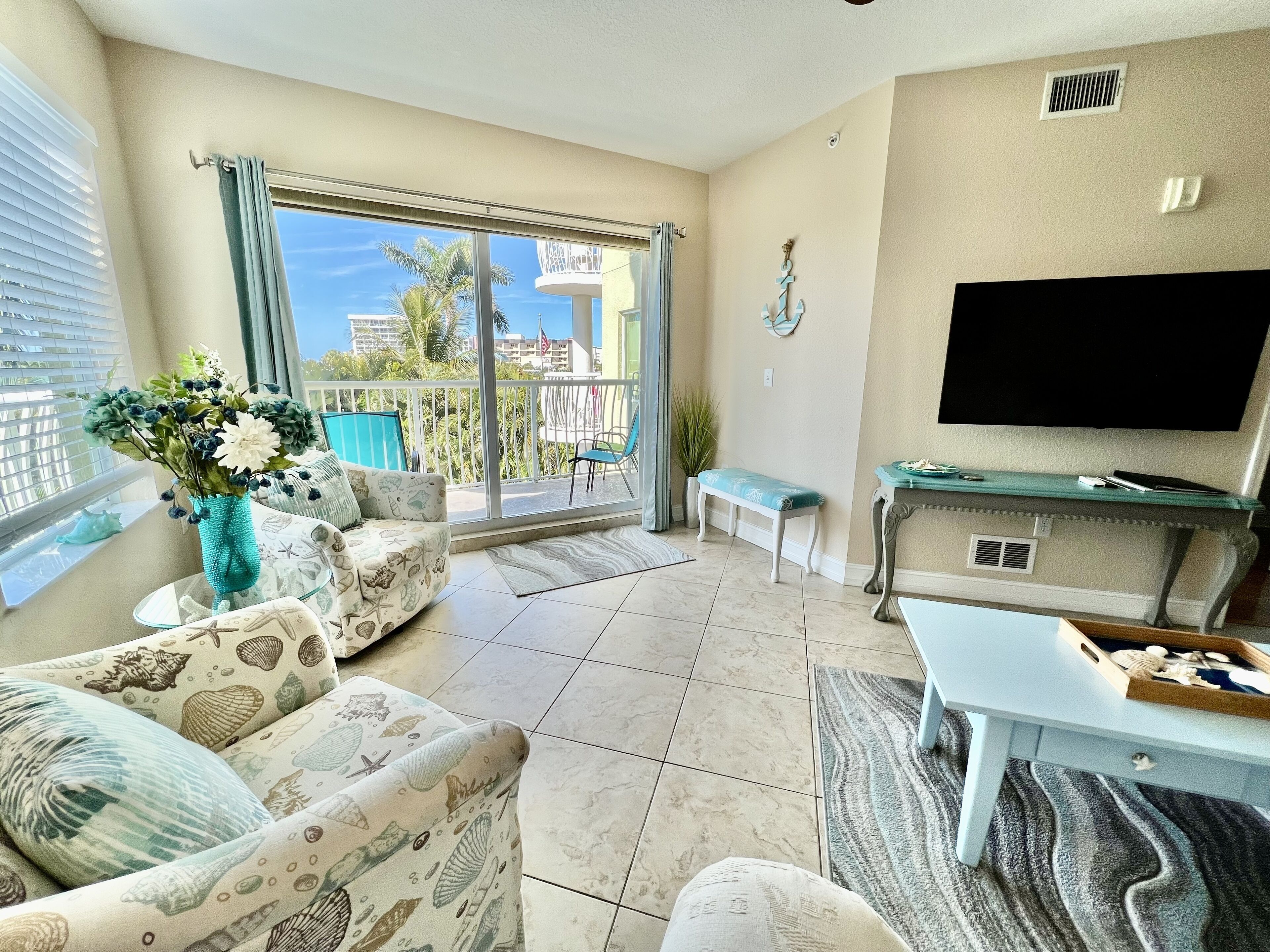 Una sala de estar con sofá, mesa de centro, televisor y balcón con vista a palmeras.