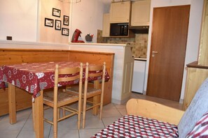 Een kleine keuken met houten kastjes, een magnetron en een eettafel met stoelen.