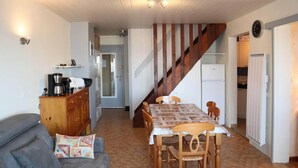 Ein gemütliches Wohnzimmer mit einer Couch, einer Kaffeestation und einem Essbereich mit Tisch und Stühlen. Eine Holztreppe führt zu einer Küchenzeile.