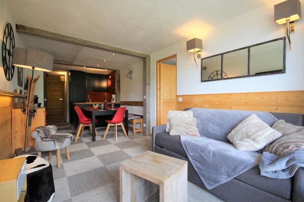 Un soggiorno accogliente con un divano grigio, un tavolino in legno e sedie rosse. C'è una zona pranzo con tavolo e sedie, e una cucina sullo sfondo.