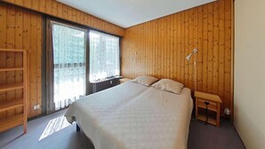 A bedroom with a large bed, wooden walls, a window with curtains, and a bedside table with a lamp. - Resort center, 2nd floor, view mountain, tv, 58m², Le Grand Bornand (Le Grand-Bornand)
