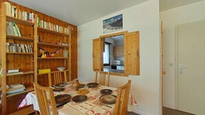 A dining area with a wooden table set for four, surrounded by bookshelves filled with books and decorative items. - Resort center, 2nd floor, view mountain, tv, 58m², Le Grand Bornand (Le Grand-Bornand)