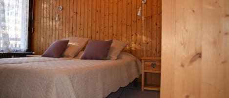 Une chambre à coucher aux murs lambrissés, comprenant un lit, deux lampes fixées au mur et une table de chevet dotée d’un tiroir.