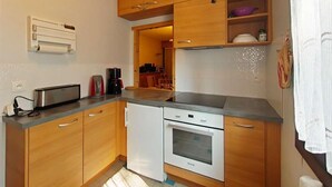 A compact kitchen with wooden cabinets, a built-in oven, and a countertop with a toaster and coffee maker. - Resort center, 2nd floor, view mountain, tv, 58m², Le Grand Bornand (Le Grand-Bornand)