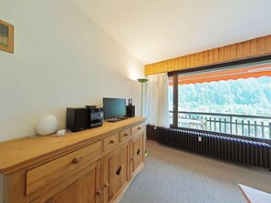 A room with a wooden dresser, a television, a speaker, and a radiator.